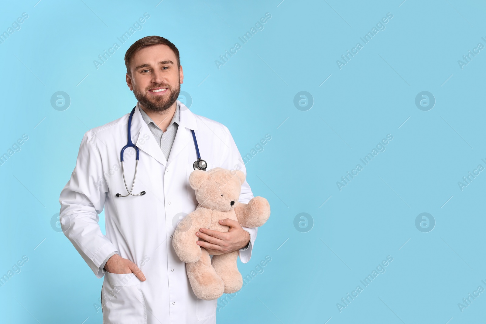 Photo of Pediatrician with teddy bear and stethoscope on light blue background, space for text