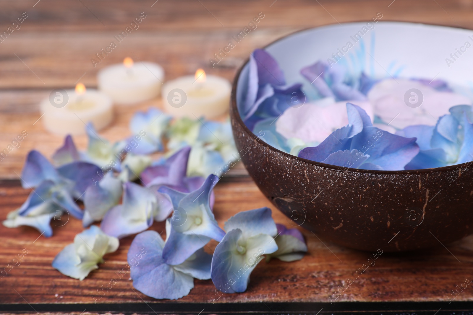 Photo of Spa composition. Aromatic water in bowl, burning candles and flowers on wooden table, closeup. Space for text