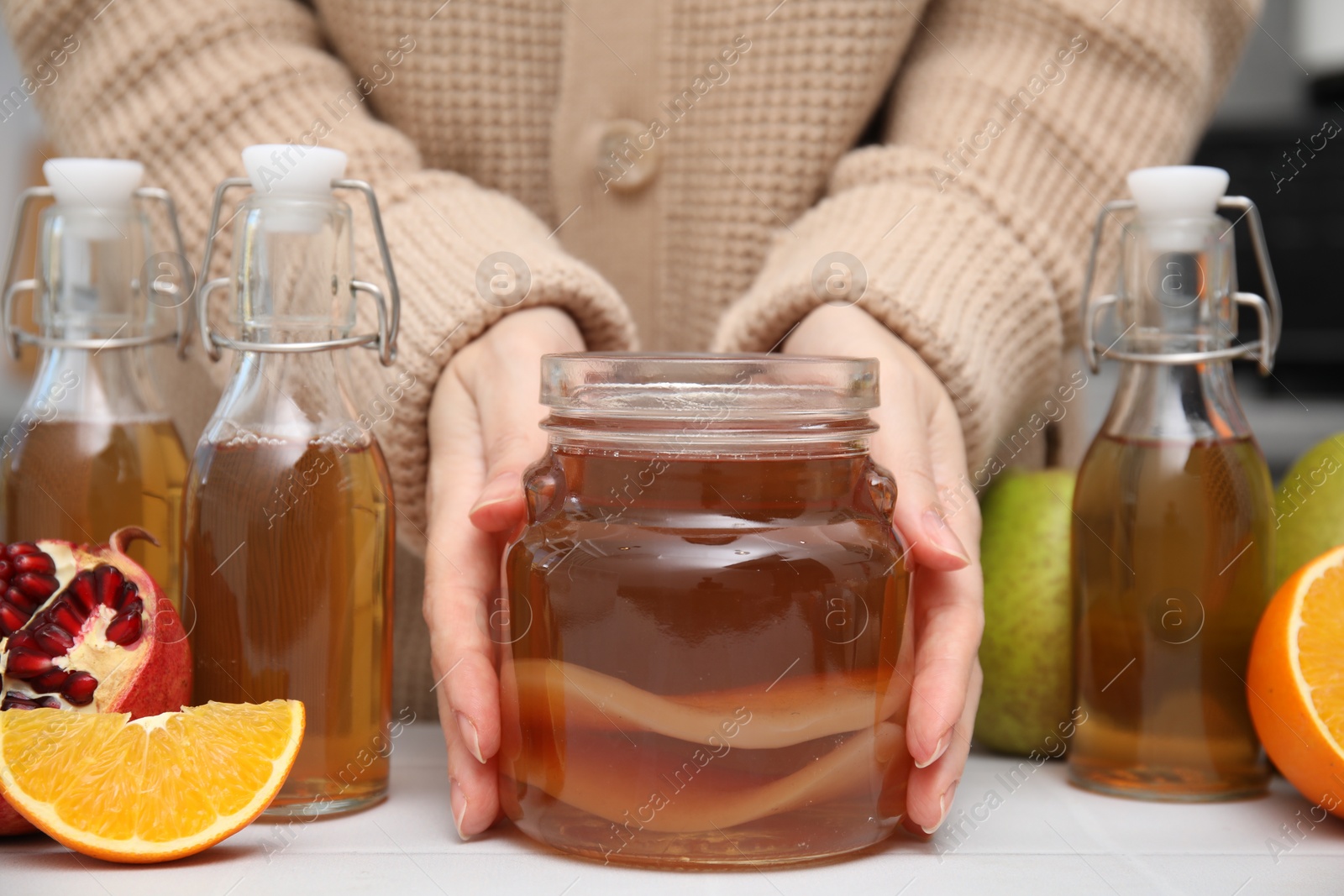 Photo of Woman taking jar of homemade fermented kombucha at white table, closeup