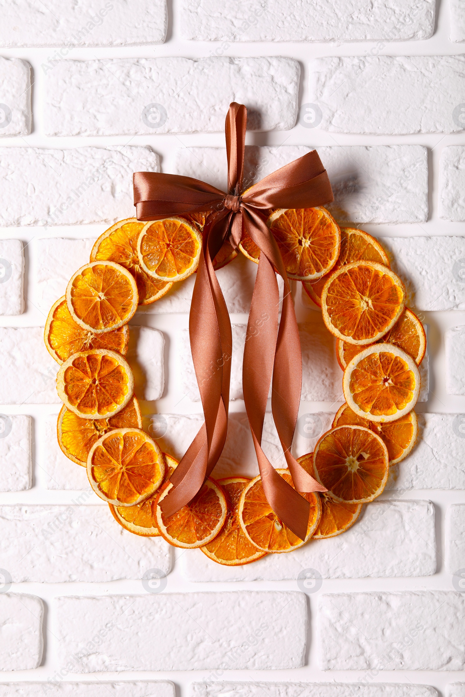 Photo of Decorative wreath made with dry oranges and ribbon hanging on white brick wall