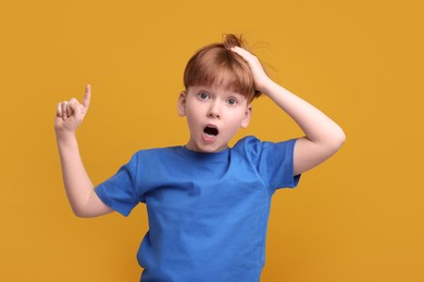 Photo of Surprised little boy pointing at something on orange background