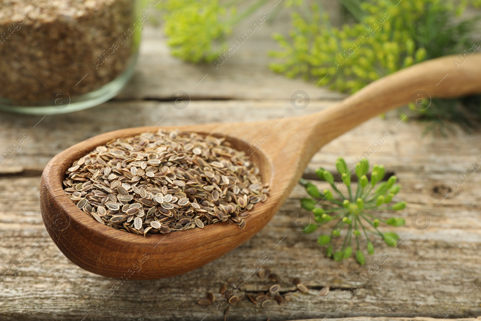 Photo of Spoon with dry seeds and fresh dill on wooden table, closeup