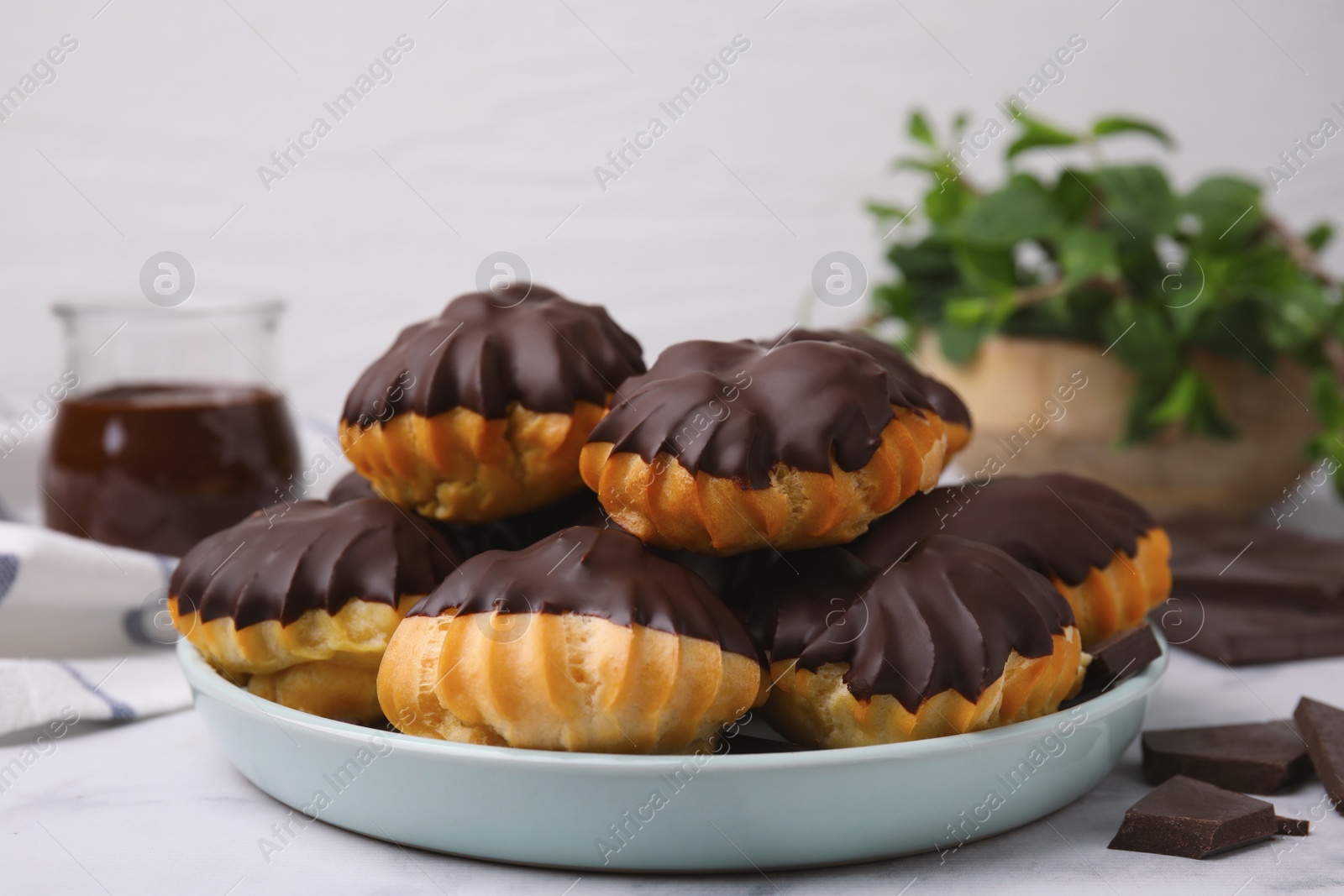 Photo of Delicious profiteroles with chocolate spread on white table, closeup