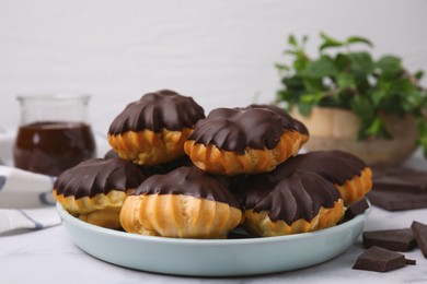 Delicious profiteroles with chocolate spread on white table, closeup