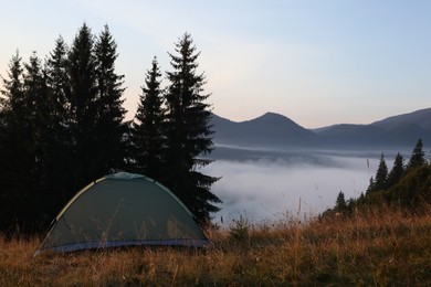 Photo of Camping tent in forest clearing near foggy mountains. Space for text