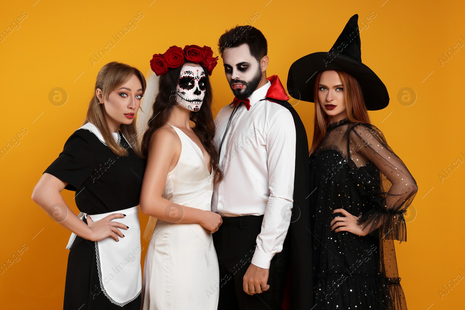 Photo of Group of people in scary costumes on orange background. Halloween celebration