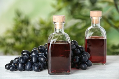 Photo of Bottles with wine vinegar and fresh grapes on wooden table against blurred background