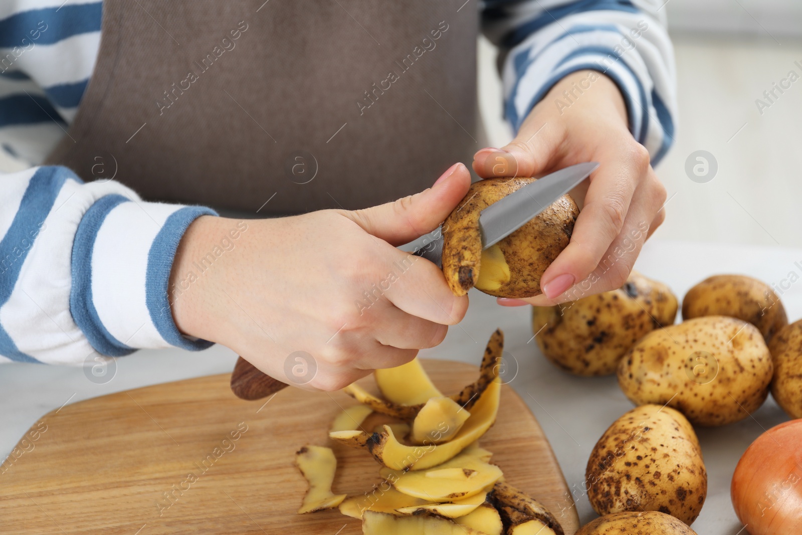 Photo of Woman peeling fresh potato with knife at table, closeup