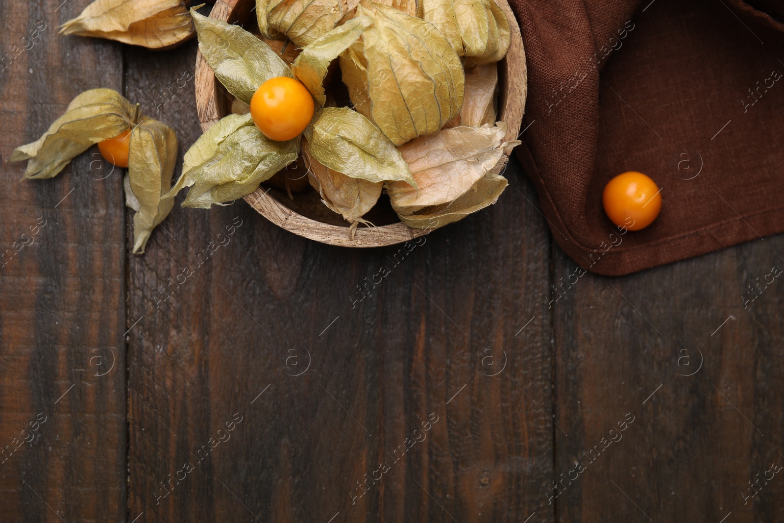 Photo of Ripe physalis fruits with calyxes in bowl on wooden table, flat lay. Space for text