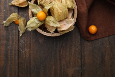 Ripe physalis fruits with calyxes in bowl on wooden table, flat lay. Space for text
