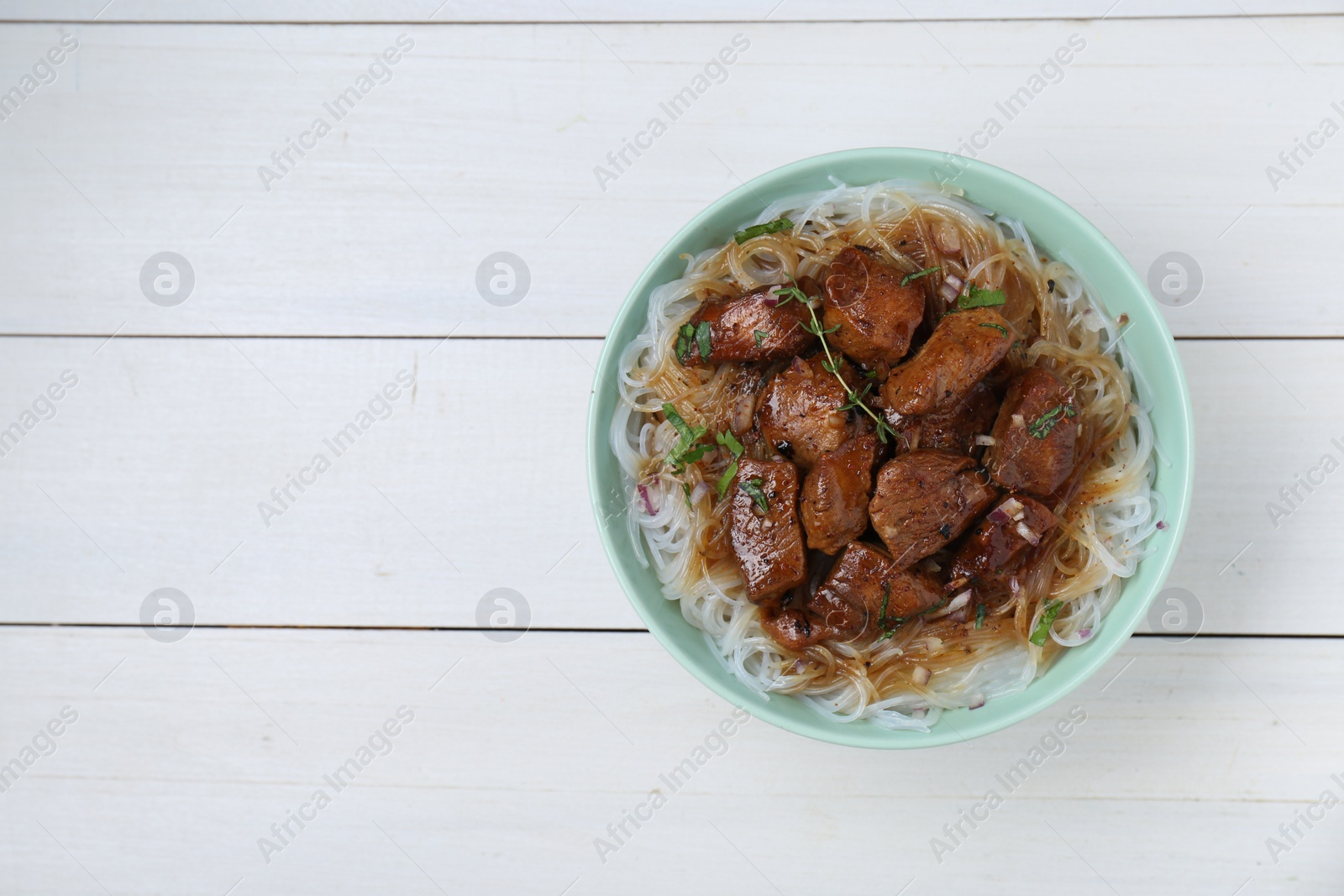 Photo of Bowl with pieces of soy sauce chicken and noodle on white wooden table, top view. Space for text