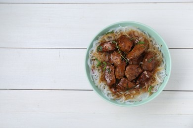 Photo of Bowl with pieces of soy sauce chicken and noodle on white wooden table, top view. Space for text