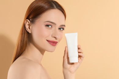 Beautiful young woman holding sun protection cream on beige background, space for text