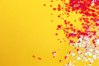 Photo of Shiny bright red glitter on yellow background. Space for text
