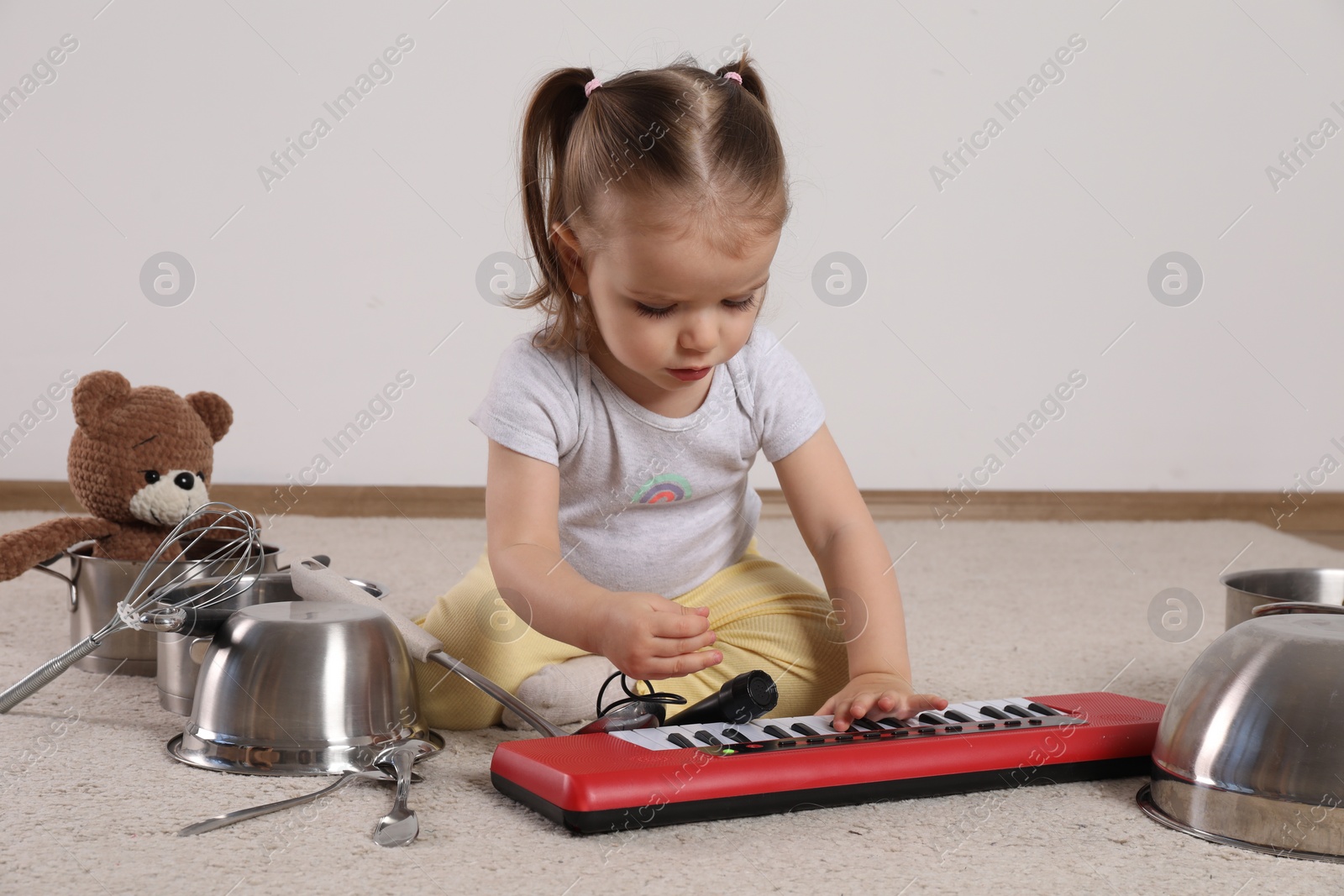 Photo of Cute little girl with cookware and toy piano at home