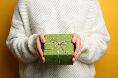 Photo of Woman holding green Christmas gift box on yellow background, closeup