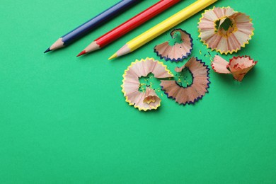 Photo of Color pencils and shavings on green background, flat lay. Space for text