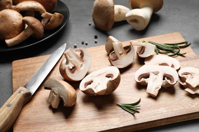Photo of Cutting board with fresh wild mushrooms and knife on grey table