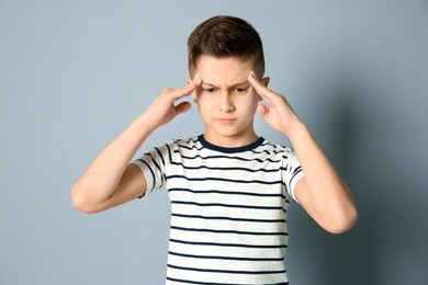 Photo of Little boy suffering from headache on grey background