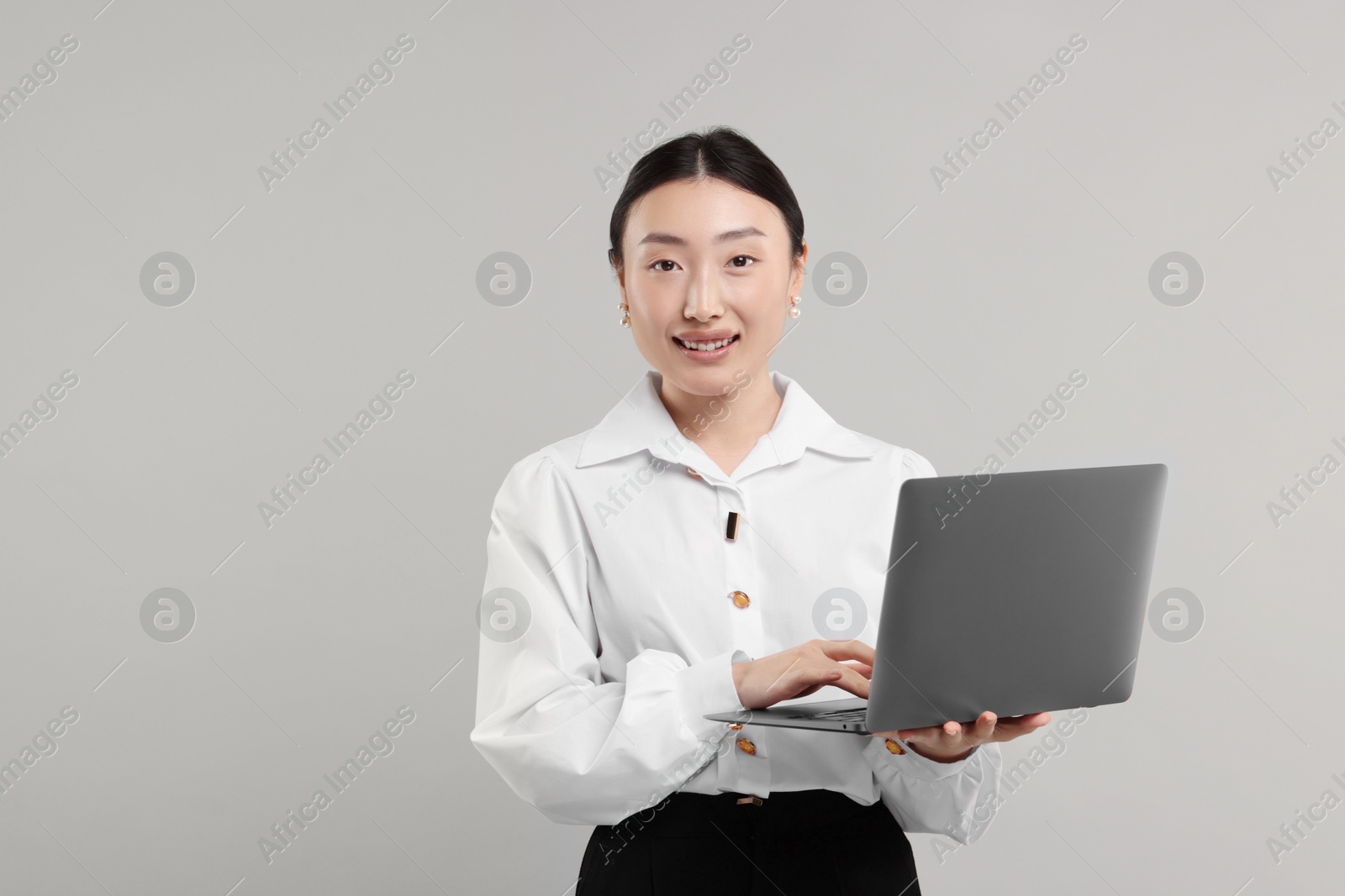 Photo of Portrait of smiling businesswoman with laptop on grey background. Space for text