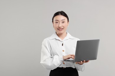 Portrait of smiling businesswoman with laptop on grey background. Space for text