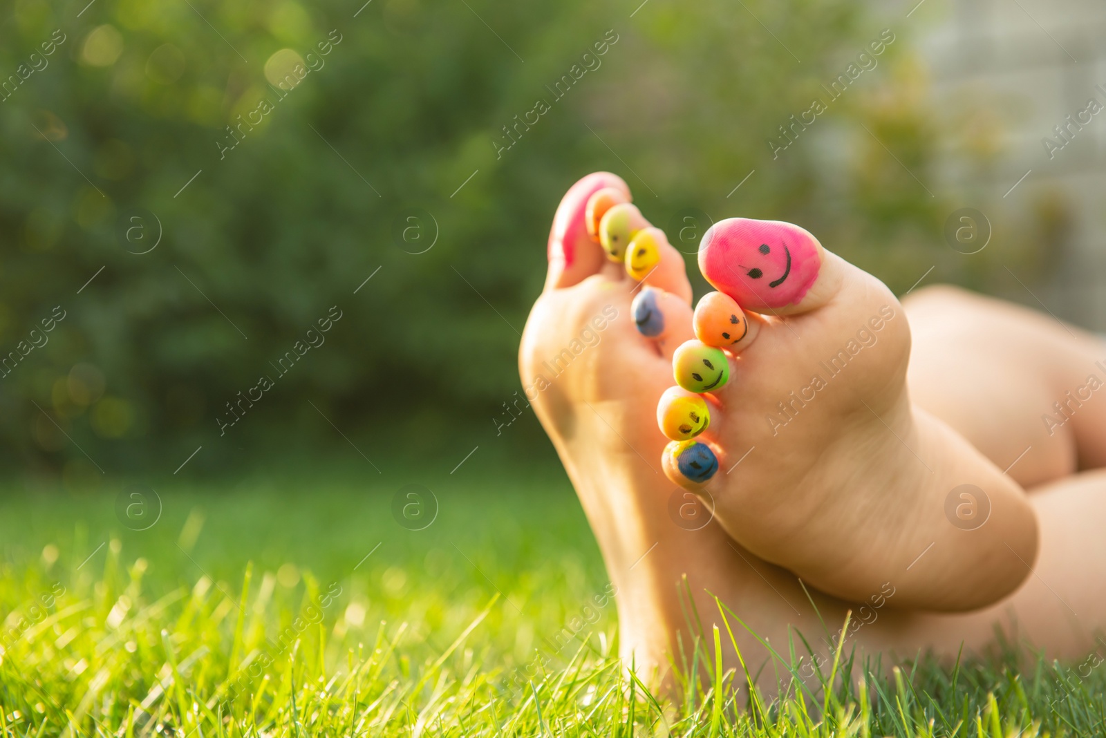 Photo of Teenage girl with smiling faces drawn on toes outdoors, closeup. Space for text