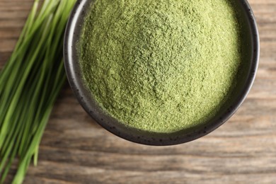 Photo of Wheat grass powder in bowl on wooden table, top view