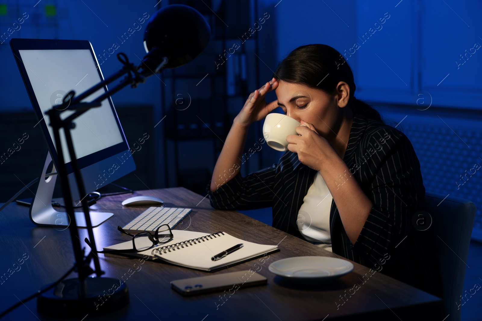 Photo of Tired overworked businesswoman drinking coffee at night in office