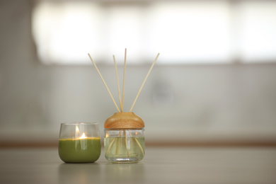 Photo of Aromatic reed air freshener and burning candle on table indoors
