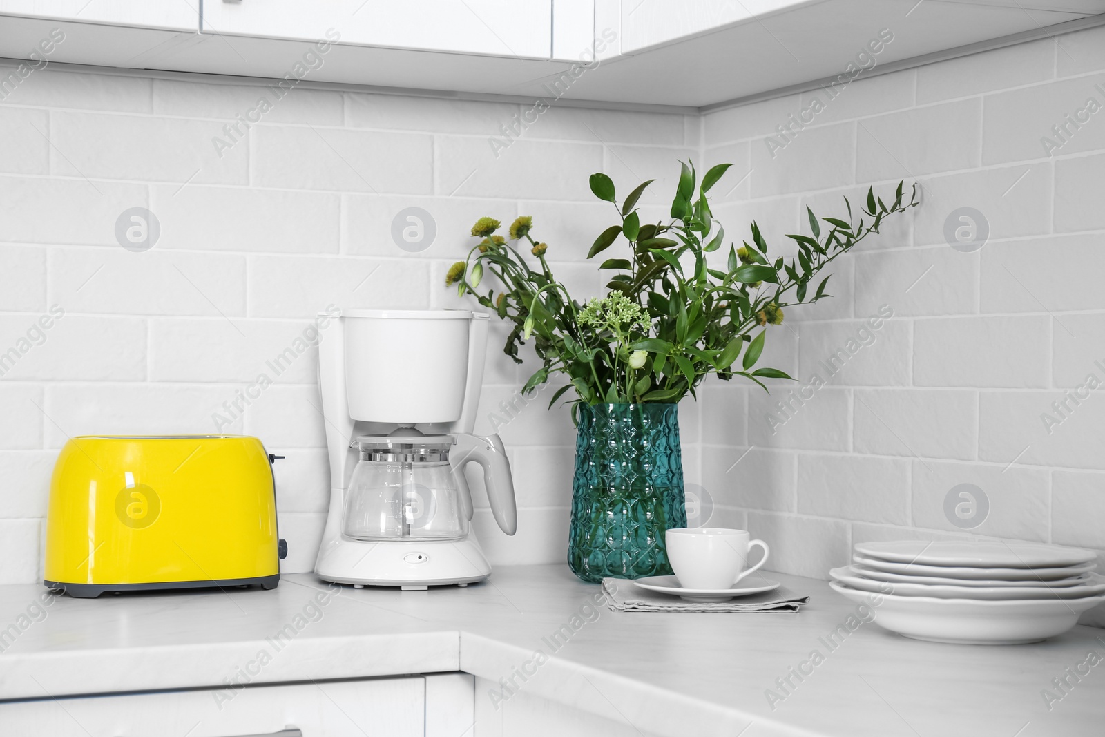 Photo of Modern yellow toaster, coffeemaker and dishware on countertop in kitchen