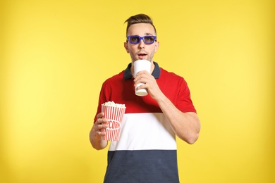 Photo of Man with 3D glasses, popcorn and beverage during cinema show on color background