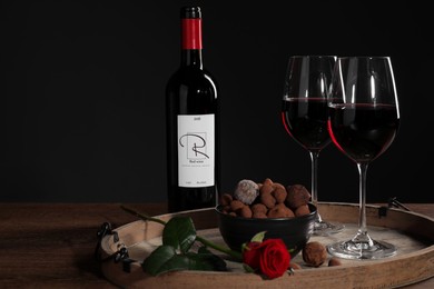 Photo of Red wine, chocolate truffles and rose flower on table against dark background