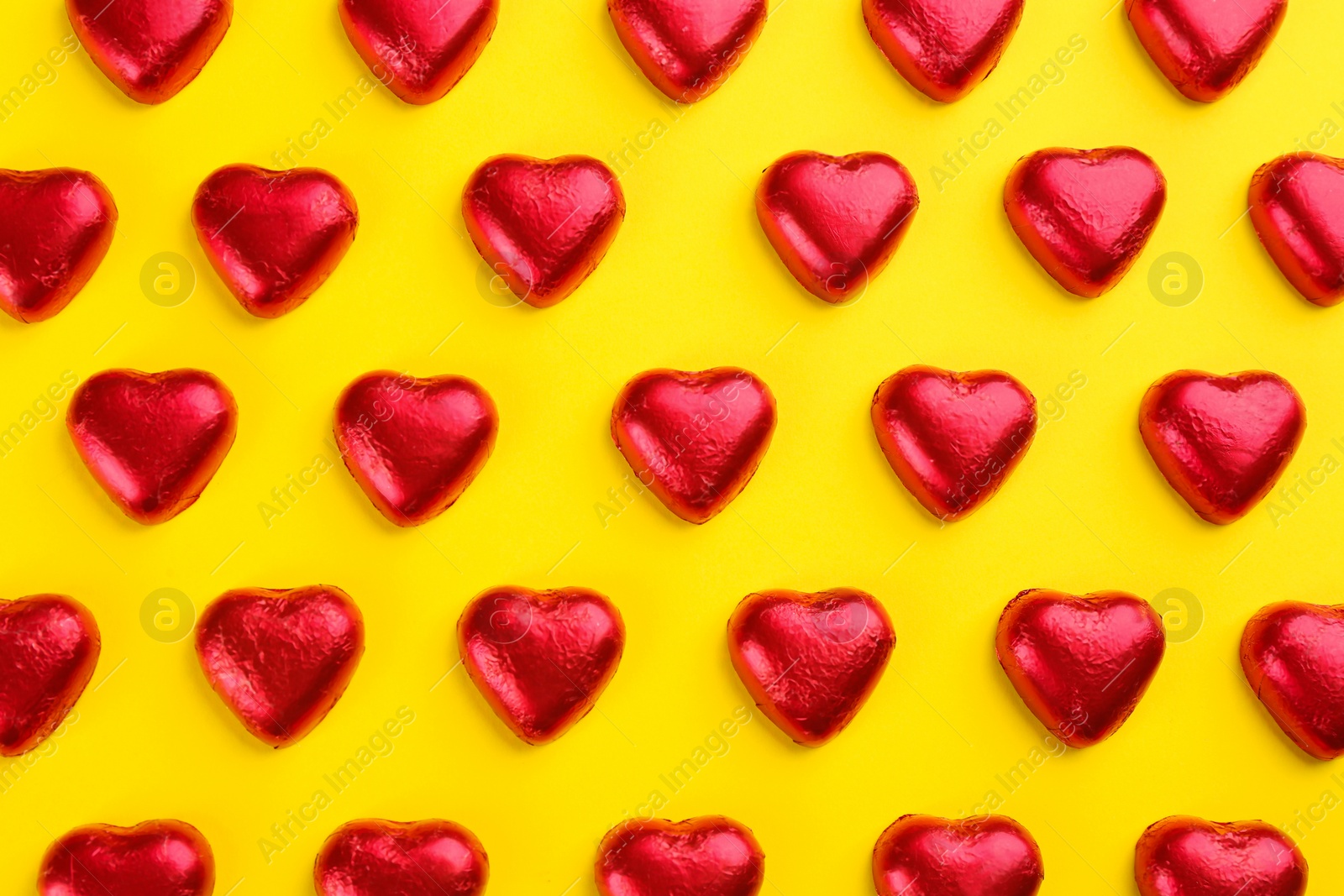 Photo of Heart shaped chocolate candies in red foil on yellow background, flat lay