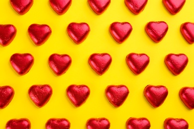 Photo of Heart shaped chocolate candies in red foil on yellow background, flat lay