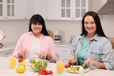 Photo of Happy overweight women having healthy meal together at table in kitchen