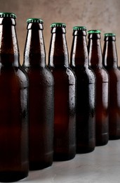 Photo of Many bottles of beer on grey table against light brown background, closeup