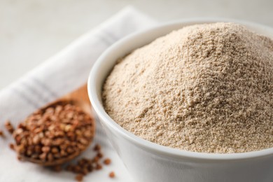 Photo of Bowl of flour and spoon with buckwheat on cloth, closeup