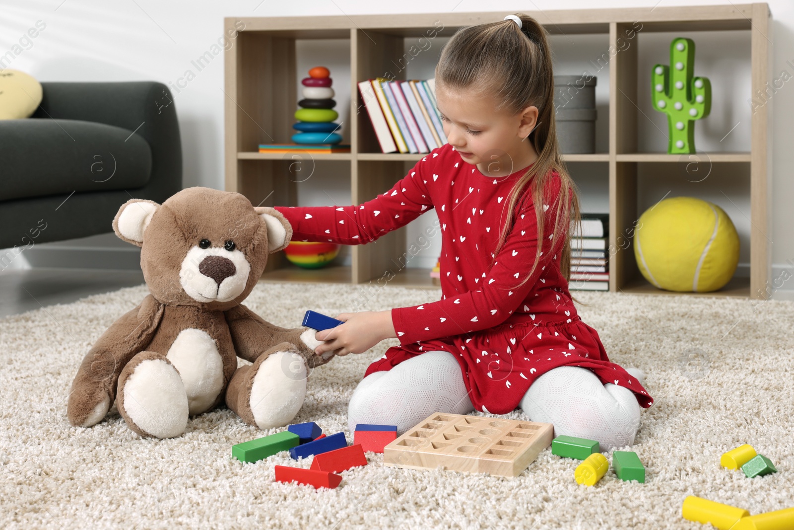 Photo of Cute little girl playing with teddy bear and cubes at home