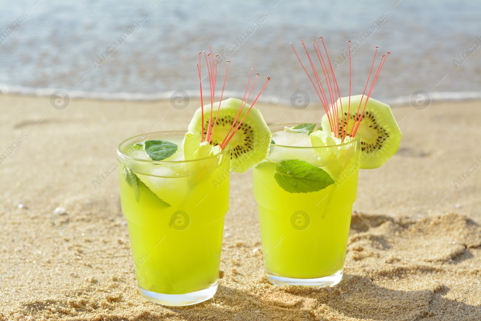 Glasses of refreshing drink with kiwi and mint on sand near sea Photo of Glasses of refreshing drink with kiwi and mint on sand near sea
