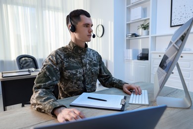 Photo of Military service. Young soldier in headphones working at wooden table in office
