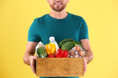 Photo of Delivery man holding wooden crate with food products on color background, closeup