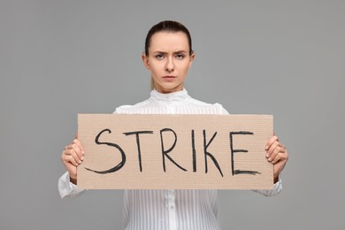 Photo of Woman holding cardboard banner with word Strike on grey background