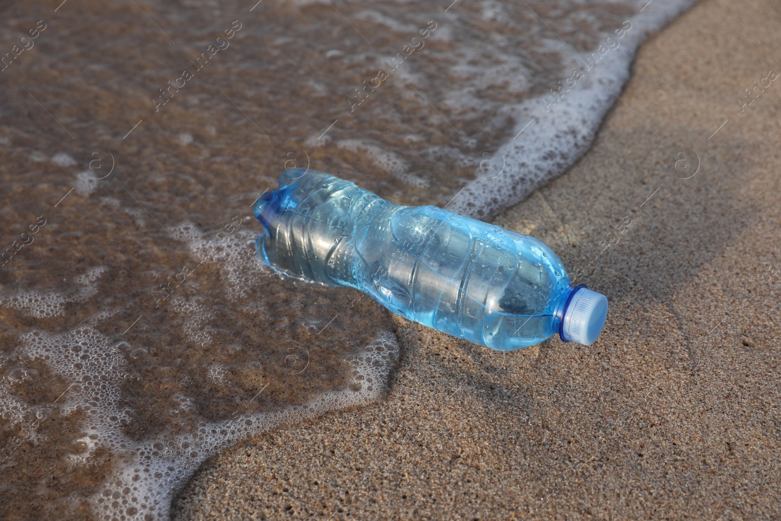Photo of Plastic bottle of fresh water on wet sand near sea
