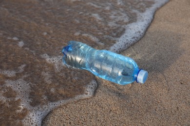 Plastic bottle of fresh water on wet sand near sea