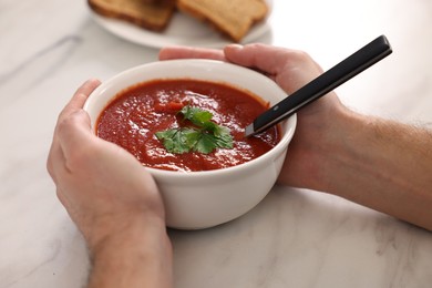 Man with delicious tomato soup at light marble table, closeup