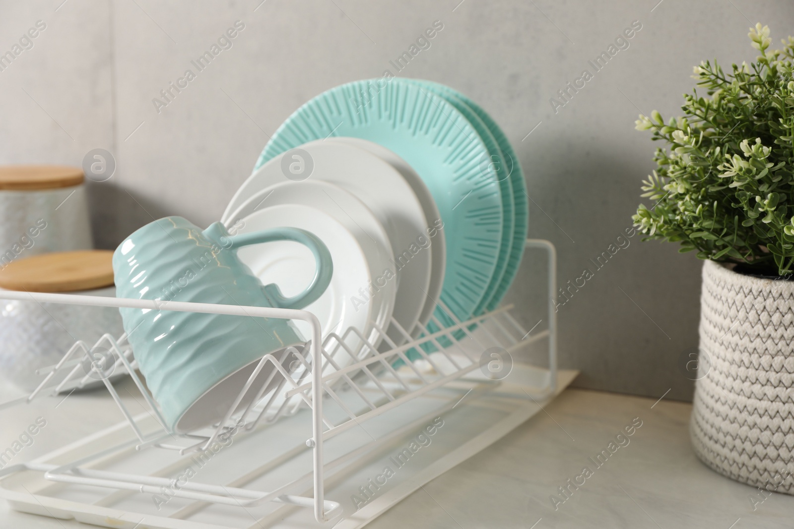 Photo of Drainer with different clean dishware and cup on light table indoors