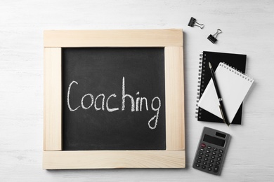 Photo of Chalkboard with word "Coaching" and stationery on wooden background. Business trainer concept