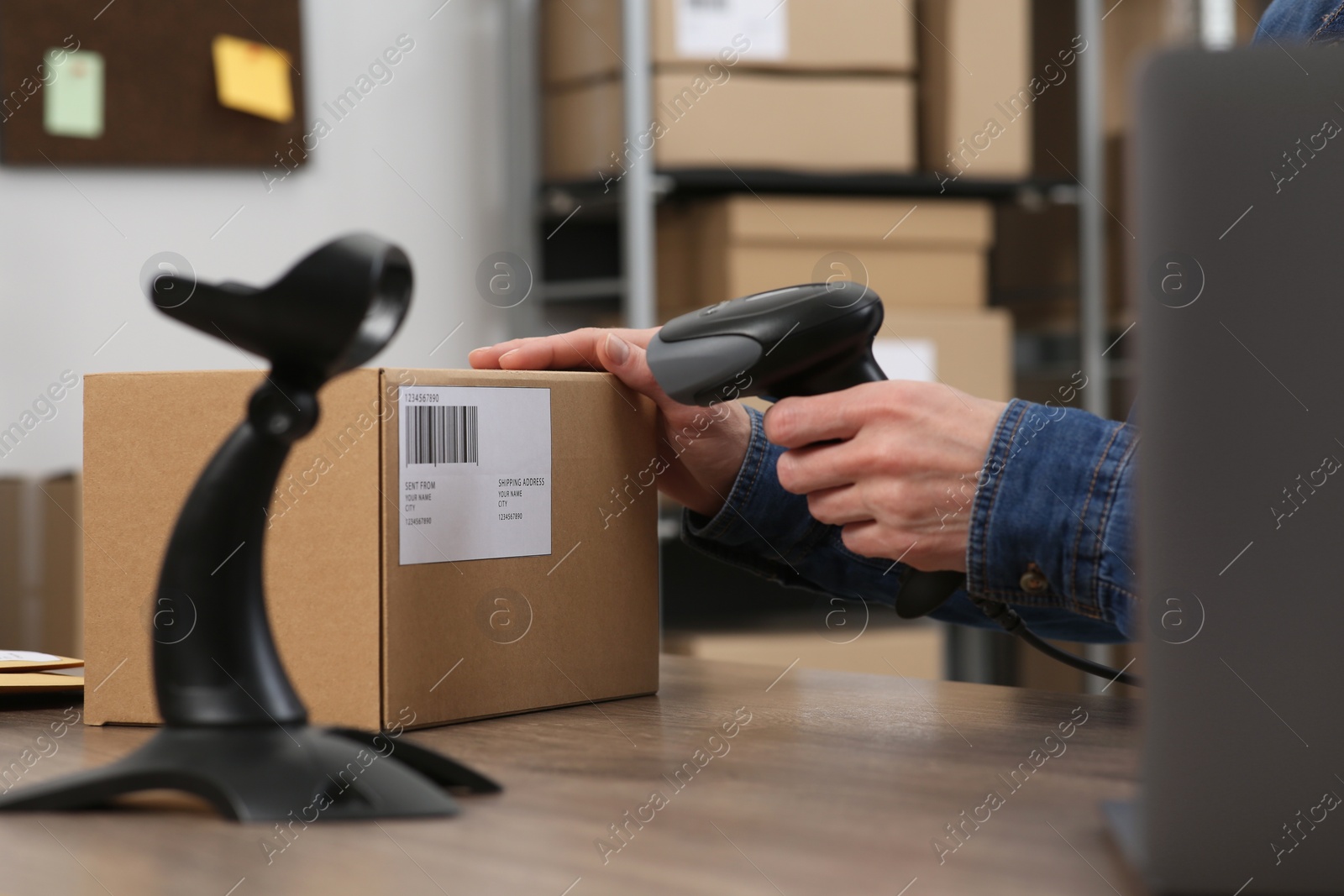 Photo of Seller with scanner reading parcel barcode at table in office, closeup. Online store