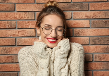 Photo of Beautiful young woman in warm sweater near brick wall