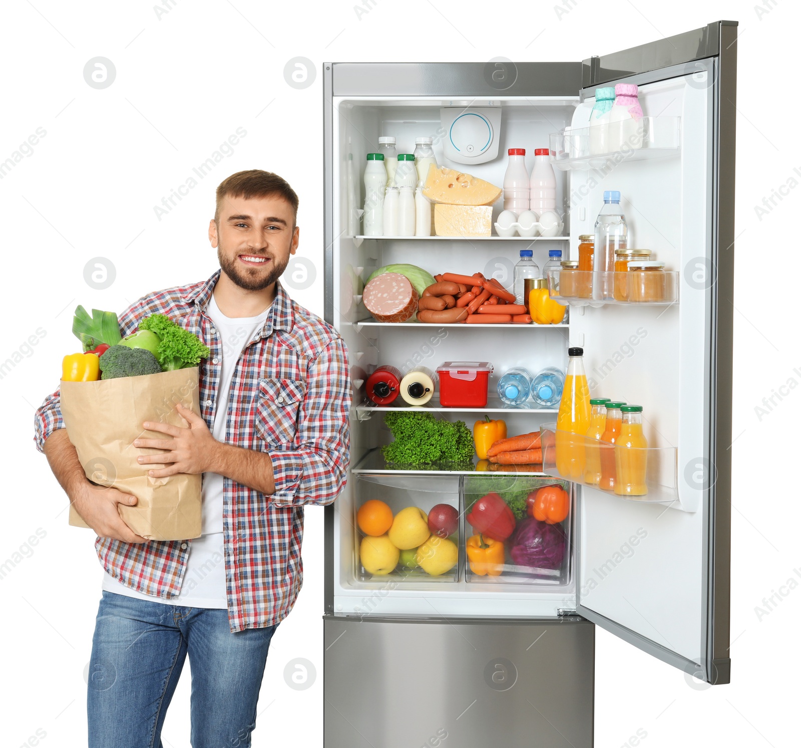 Photo of Young man with bag of groceries near open refrigerator on white background